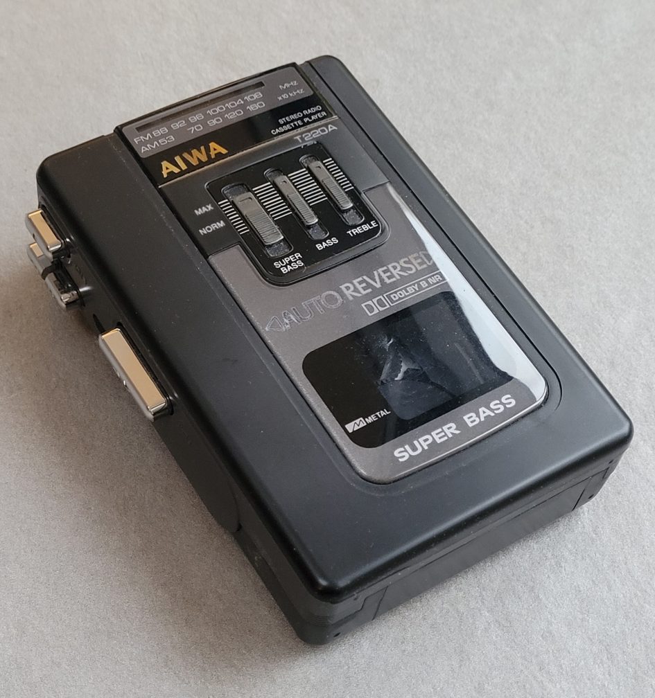 Shows the Aiwa T220A front controls with 3 sliders for super bass, bass and treble along with the usual play controls along with a reverse tape slide switch on the side.