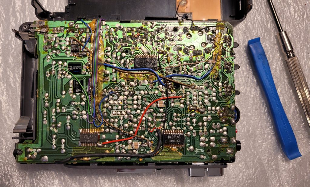 Image shows the single PCB inside the Aiwa along with the pry tool and cross head driver.