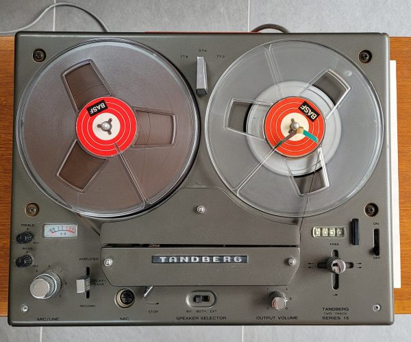 Shows the Tandberg series 15's top deck loaded with 7" BASF tape. Rotary controls left to right for treble and bass, input level (mic + line), amplifier lever switch (external, playback, record), stop lever, volume, operation lever, tape counter reset and on/off lever far right.