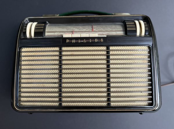 Front view of Philips Babette Radio showing three column golden speaker grille with two pairs of large thumbwheel controls for FM and AM tuning on left and volume & tone to the right. An un-illuminated tuning dial centre top with a row of pushbuttons below.